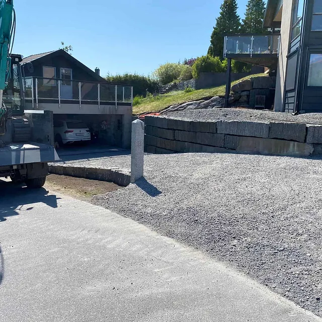 Ny gruslagt innkjørsel foran hus med støttemur og parkert gravemaskin.